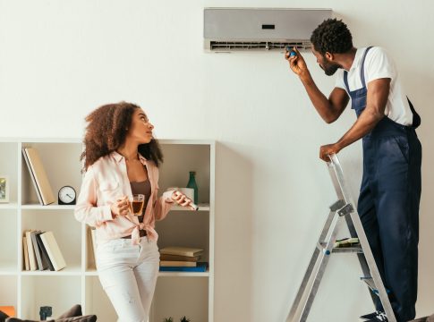 african american repairman fixing air conditioner near pretty african american woman holding remote controller