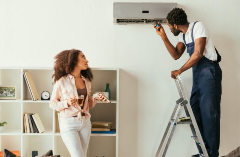 african american repairman fixing air conditioner near pretty african american woman holding remote controller