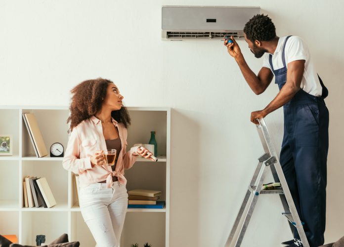 african american repairman fixing air conditioner near pretty african american woman holding remote controller