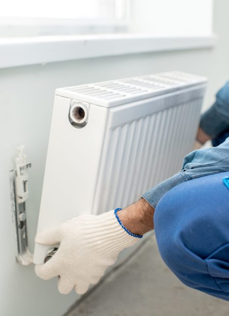 Workman mounting water heating radiator on the white wall indoors, close-up view