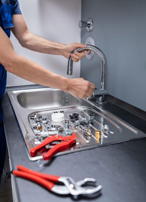 Happy Young Male Plumber Fixing Faucet In Kitchen