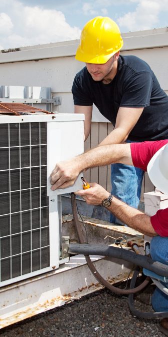 Two workers on the roof of a building working on the air conditioning unit.