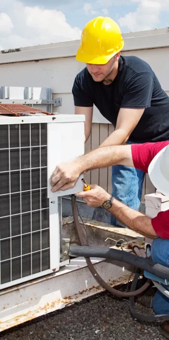Two workers on the roof of a building working on the air conditioning unit.