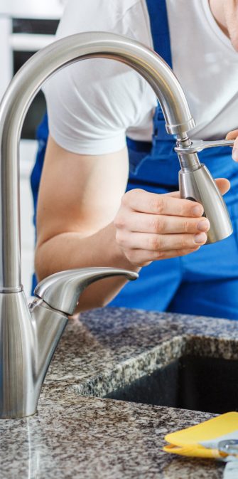 Close-up of smiling plumber fixing a faucet with blue pipes on the countertop