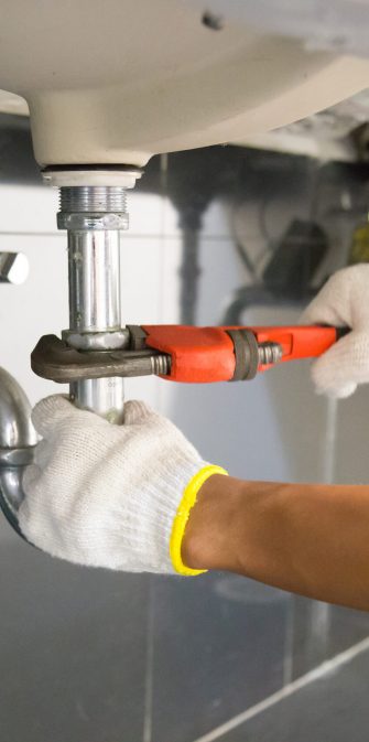 Plumber fixing white sink pipe with adjustable wrench.