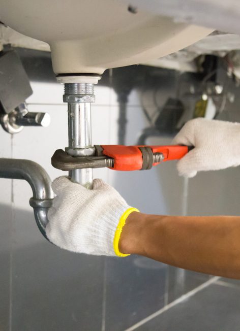 Plumber fixing white sink pipe with adjustable wrench.