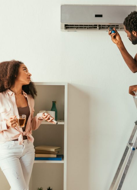 african american repairman fixing air conditioner near pretty african american woman holding remote controller